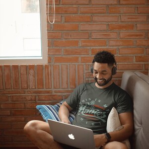 May include: A person wearing a dark green t-shirt with the text "This is my movies shirt" and a film reel graphic. The person is sitting on a sofa with a laptop on their lap and headphones on their head.