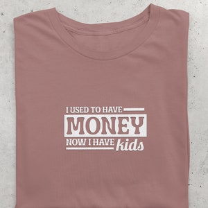 May include: A mauve t-shirt with the text "I used to have money now I have kids" printed in white.
