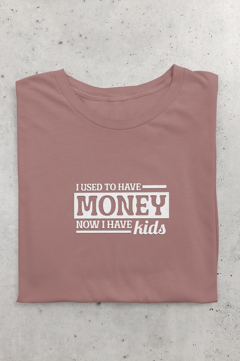 May include: A mauve t-shirt with the text "I used to have money now I have kids" printed in white.