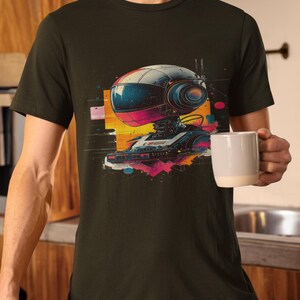 May include: A dark green t-shirt with a graphic print of a robot with a helmet and a camera. The robot is surrounded by colorful geometric shapes and splatters of paint.