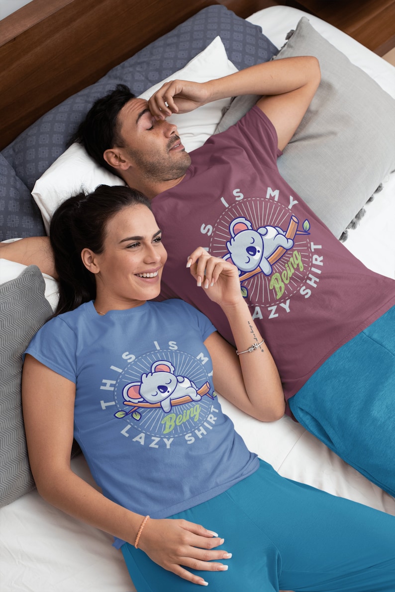 以下が含まれることがあります： 「This is my being lazy shirt」というテキストとコアラのグラフィックがプリントされた、ブルーとマルーンのペアのTシャツを着たカップルです。