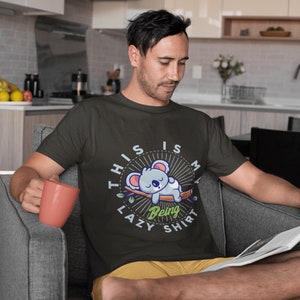 以下が含まれることがあります： 寝ているコアラのグラフィックと「This is my lazy being shirt」というテキストが書かれた黒いTシャツ。