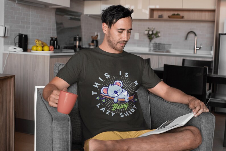 以下が含まれることがあります： 寝ているコアラのグラフィックと「This is my lazy being shirt」というテキストが書かれた黒いTシャツ。