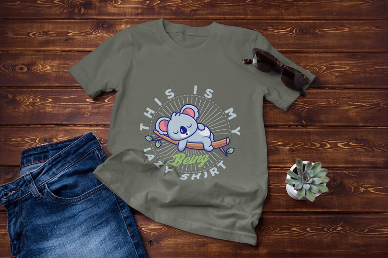 以下が含まれることがあります： 枝で眠る漫画のオウムのイラストが描かれた緑色のTシャツ。Tシャツには「This is my lazy being shirt」という文字が書かれています。