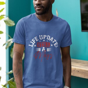 以下が含まれることがあります： 白い文字と赤い文字で「Life Update: Still a Mess」と書かれた青いTシャツ。テキストは星とストライプで囲まれています。