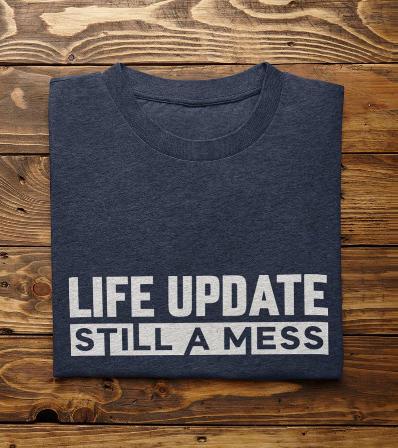 May include: A navy blue t-shirt with the text "LIFE UPDATE STILL A MESS" printed in white.