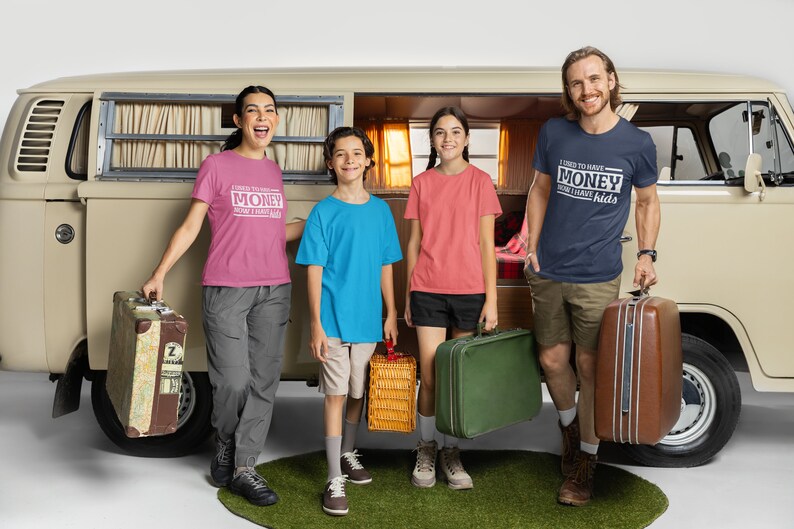 May include: A family of four standing in front of a vintage van, each wearing a t-shirt with a humorous saying. The shirts say "I used to have money, now I have kids". The family is holding luggage and a picnic basket, suggesting they are going on a trip.