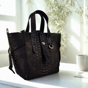 Peut inclure: Un sac cabas noir en cuir de serpent avec une poignée supérieure et une boucle argentée.