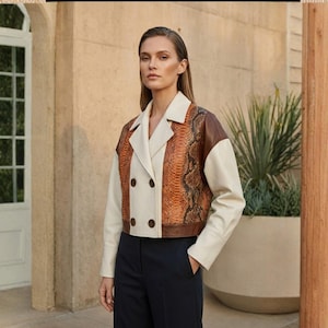 Könnte beinhalten: Eine kurze Jacke mit einem Schlangenmuster-Frontpanel, braunen Ärmeln und einem cremefarbenen Körper. Die Jacke hat ein doppelreihiges Design und wird mit einer marineblauen Hose kombiniert.