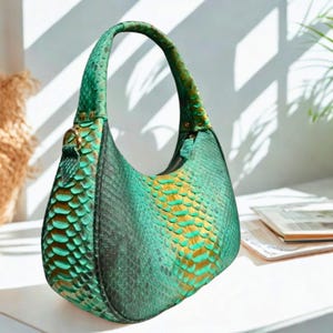Peut inclure: Un sac à main en cuir de serpent vert et or avec une forme incurvée et une seule poignée supérieure.