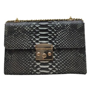 Puede incluir: Un bolso bandolera de piel de serpiente negra con cierre dorado y cadena.