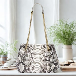 Könnte beinhalten: Eine kleine, weiße und schwarze Schlangenleder-Handtasche mit einer goldenen Kettenkette.