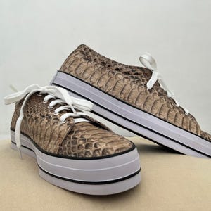 Op de afbeelding: Een paar bruine slangenleren sneakers met witte veters en een witte rubberen zool.