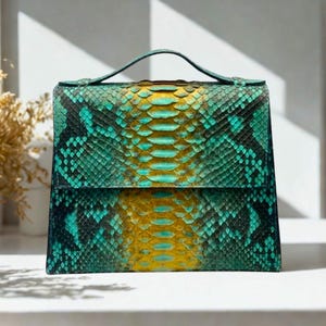 Puede incluir: Bolso de mano rectangular con asa superior, elaborado con un patrón de piel de serpiente en tonos turquesa, amarillo y negro. El bolso presenta un cierre de solapa y un diseño estructurado.