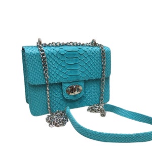 Puede incluir: Un bolso de hombro de piel de serpiente azul turquesa con una correa de cadena plateada y un cierre plateado.