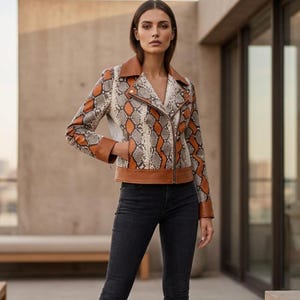 May include: A snakeskin-patterned leather jacket with brown and tan accents. The jacket features a notched collar, a diagonal zipper, and brown leather trim. The model is wearing black jeans.