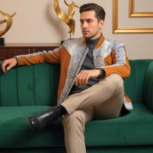 Może przedstawiać: Brązowa i szara skórzana kurtka ze wzorem wężowej skóry na rękawach i ramionach. Kurtka jest noszona na szarym golfie. Osoba siedzi na zielonej aksamitnej kanapie.