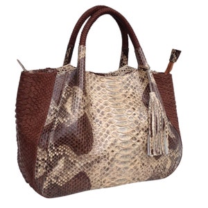 May include: A brown and beige snakeskin tote bag with a tassel. The bag has a top handle and a zip closure.