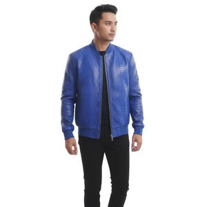 Puede incluir: Chaqueta bomber azul brillante con un patrón texturizado similar a la piel de serpiente. La chaqueta tiene cierre de cremallera frontal, puños de canalé y dobladillo de canalé a juego. El modelo lleva pantalones negros. Una opción de abrigo elegante.