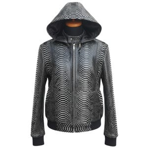 Pode incluir: Casaco com capuz com padrão preto e branco com fecho de correr. O casaco tem um design semelhante a pele de cobra e é exibido em um manequim. Possui bainha e punhos canelados pretos.