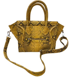 Könnte beinhalten: Eine gelbe Schlangenleder-Handtasche mit einem oberen Henkel und einem langen Schulterriemen.