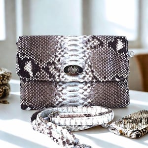 Puede incluir: Un pequeño bolso de mano de piel de serpiente marrón y blanco con un cierre plateado. El bolso tiene una correa a juego de piel de serpiente.