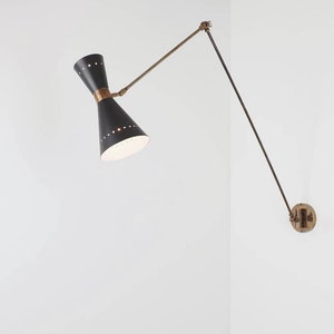 May include: A black and brass wall-mounted light fixture with an adjustable arm. The light has a cone-shaped shade with a white interior and a brass accent ring.
