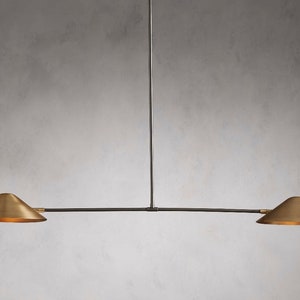 May include: A modern, minimalist light fixture with two brass shades and a black metal frame. The shades are angled downwards, creating a focused light source.
