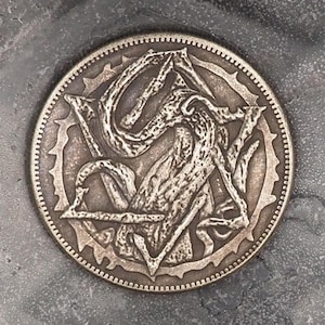 May include: A silver coin with a detailed design of an octopus inside a six-pointed star.