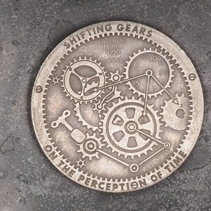 May include: A silver-toned metal disc with the words "Shifting Gears on the Perception of Time" and an intricate design of gears.