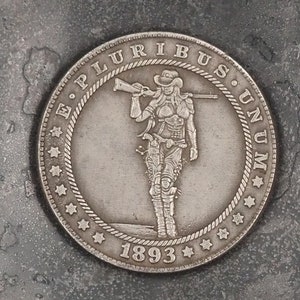 May include: A silver coin with a woman holding a rifle and the words "E. Pluribus Unum" and "1893" on it.