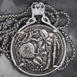 Könnte beinhalten: Silberne Anhänger Halskette mit detailliertem Reliefdesign. Der Anhänger zeigt eine Szene mit Figuren und dem Jahr 1921. Die Halskette hat eine Kette mit dekorativem Verschluss, alles in Silber.