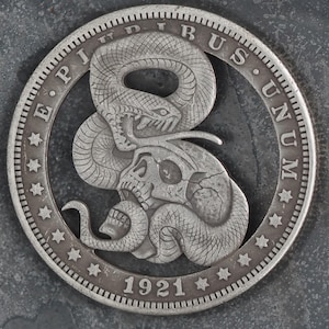Op de afbeelding: Een zilveren munt met een slang die om een schedel is gewikkeld. De munt heeft de inscripties "E. Pluribus Unum" en "1921".