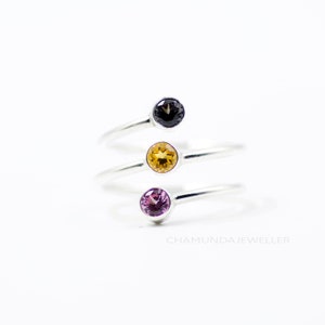 Peut inclure: Trois bagues en argent avec des pierres précieuses de différentes couleurs. La bague du haut a une pierre noire, la bague du milieu a une pierre jaune et la bague du bas a une pierre violette.