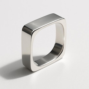 Puede incluir: Un anillo plateado pulido con diseño cuadrado. El anillo tiene esquinas redondeadas y una superficie lisa y reflectante. Una pieza de joyería minimalista.