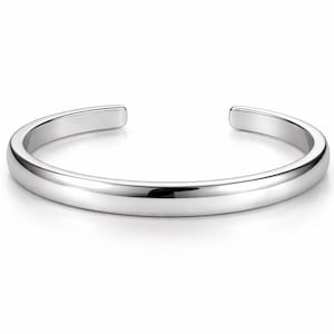 Puede incluir: Un brazalete de plata pulida con un diseño redondeado. El brazalete abierto tiene una superficie lisa y reflectante, y se muestra sobre un fondo blanco. Esta joya minimalista es adecuada para el uso diario.