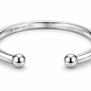 May include: A polished silver cuff bracelet with rounded ends. The open design features a smooth, curved band with a small ball at each end. The bracelet is stamped with "925" and a small symbol.