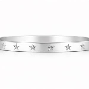 Op de afbeelding: Een zilverkleurige armband met een reeks sterren in reliëf. De armband heeft een gladde, gepolijste afwerking en een eenvoudig, elegant ontwerp. De sterren zijn gelijkmatig verdeeld. De diameter is ongeveer 6,5 cm.
