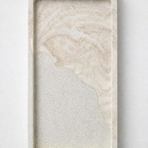 Op de afbeelding: Rechthoekige decoratieve tray met een tweekleurig ontwerp. De tray heeft aan één kant een lichtbeige marmerachtig patroon en aan de andere kant een gespikkeld grijs oppervlak. De tray heeft een opstaande rand.