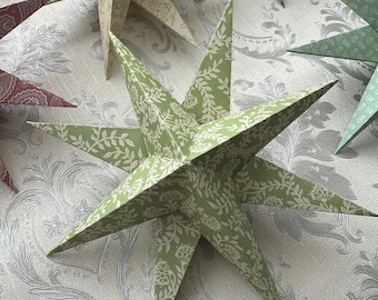 Puede incluir: Una colección de seis estrellas de papel con un patrón floral verde y blanco. Las estrellas están dispuestas en un círculo sobre un fondo plateado con patrones.