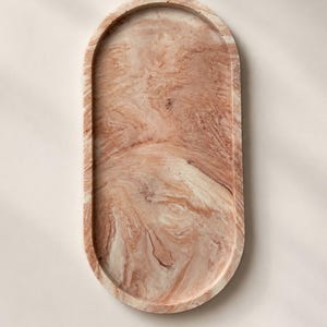 K&ouml;nnte beinhalten: Ovale Dekoschale mit Marmormuster in Rosa-, Beige- und Braunt&ouml;nen. Die Schale hat eine glatte, polierte Oberfl&auml;che und einen erh&ouml;hten Rand. Das Design &auml;hnelt Naturstein oder einem Aquarelleffekt. Ideal zum Pr&auml;sentieren kleiner Gegenst&auml;nde.