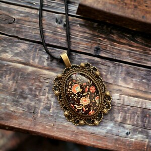 May include: A gold-toned oval pendant necklace with a black and floral patterned cameo. The cameo is set in a detailed ornate frame.