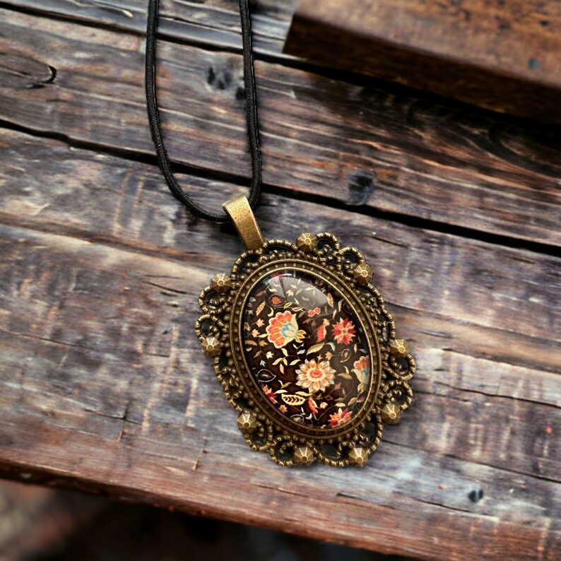 May include: A gold-toned oval pendant necklace with a black and floral patterned cameo. The cameo is set in a detailed ornate frame.