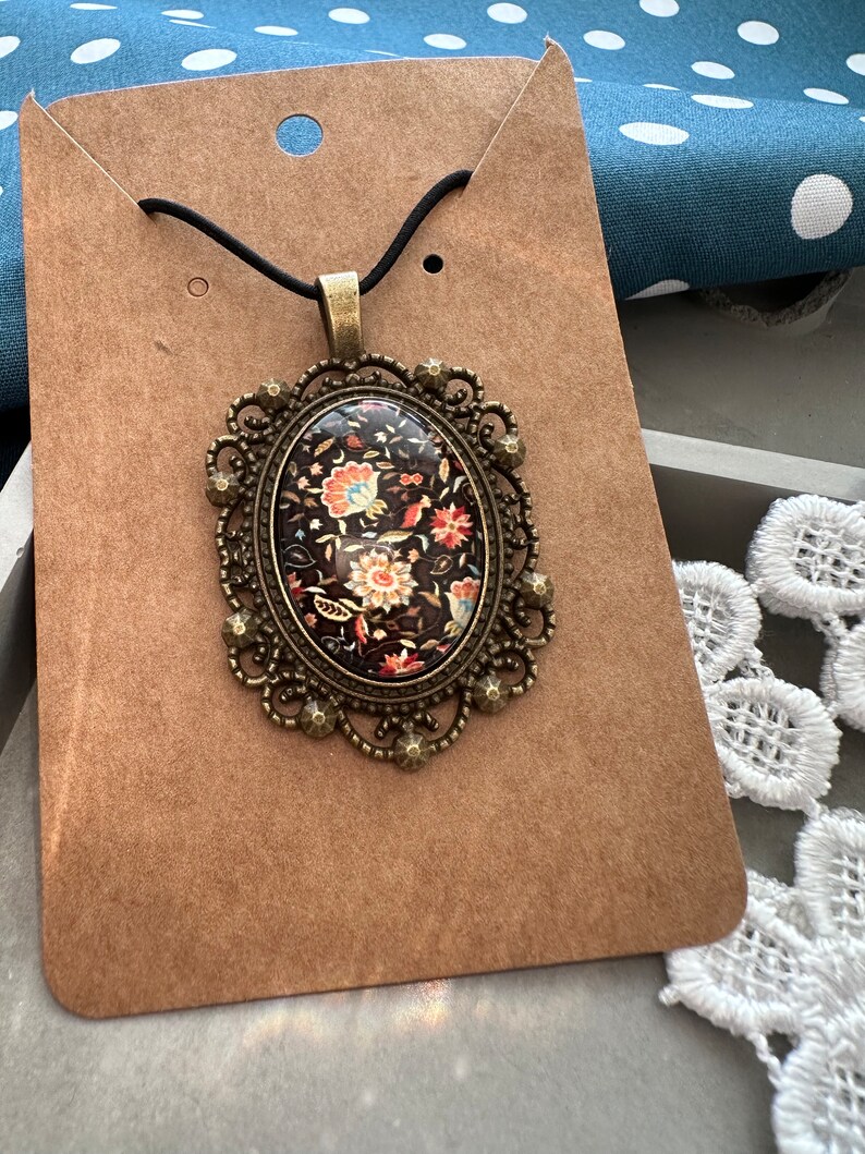 May include: A vintage-style pendant necklace featuring a black and brown cameo with a floral design. The cameo is set in a gold-toned metal frame with intricate details.