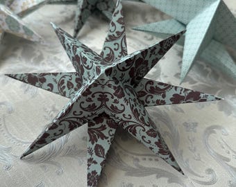 Puede incluir: Una estrella de papel azul verdoso y marrón con un patrón de damasco. La estrella está doblada y tiene una forma tridimensional.