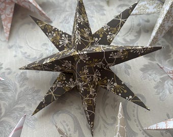 Puede incluir: Una colección de estrellas de papel en varios colores y patrones, incluyendo marrón con diseños florales blancos, rosa con un patrón de damasco y blanco con un patrón de damasco dorado. Las estrellas están dobladas y tienen una apariencia tridimensional.