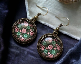May include: A pair of bronze earrings with pink and green floral patterns inside glass cabochons.