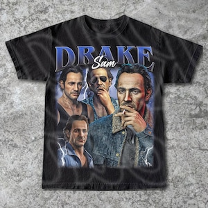 May include: Black t-shirt with a vintage-style graphic of four men's faces. The text "Drake Sam" is printed in blue above the faces.