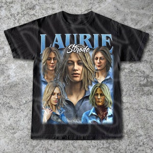 May include: Black t-shirt with a vintage-style graphic of Laurie Strode from the Halloween franchise. The graphic features multiple images of Laurie Strode, with the text "Laurie Strode" in a white font.