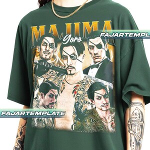 May include: Dark green t-shirt featuring a graphic of a man with an eyepatch, with the text "MAJIMA Goro" in gold lettering. The design includes multiple images of the same character in various poses. The shirt has a crew neck and short sleeves.